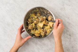 Person stirring potato salad in a bowl